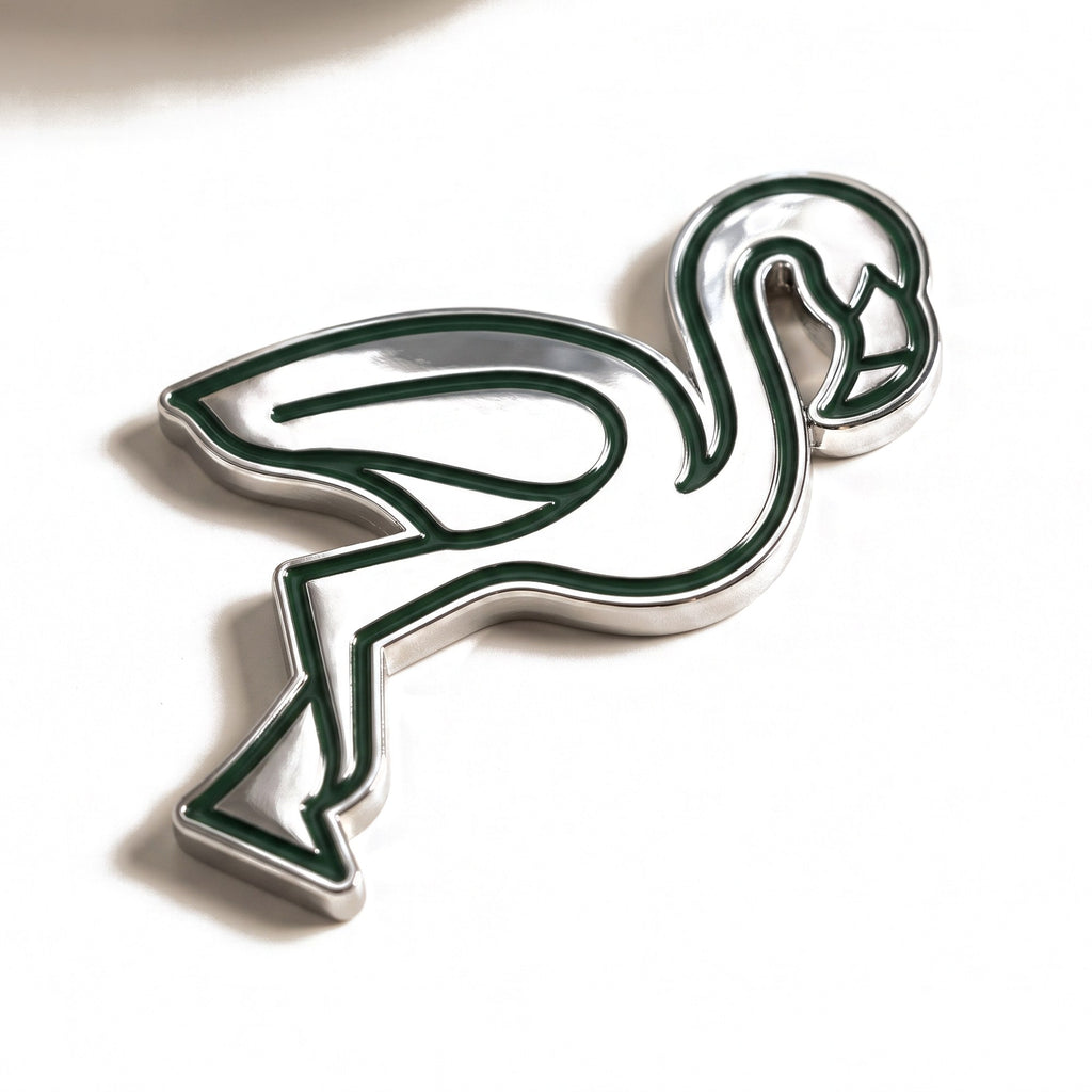The Flamingo golf ball marker, a polished chrome flamingo silhouette with recessed forest green line work, photographed at an angle.