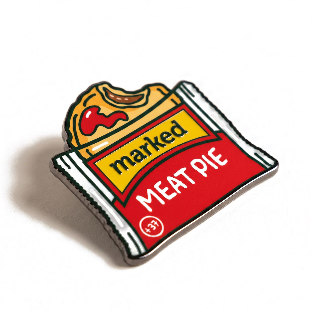 The Meat Pie golf ball marker, a die-cut badge shaped like a wrapped pie with a red wrapper and yellow marked label, photographed at an angle.