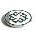 The Monogram golf ball marker, a round polished chrome disc with an interlocking M in recessed forest green enamel, photographed at an angle.