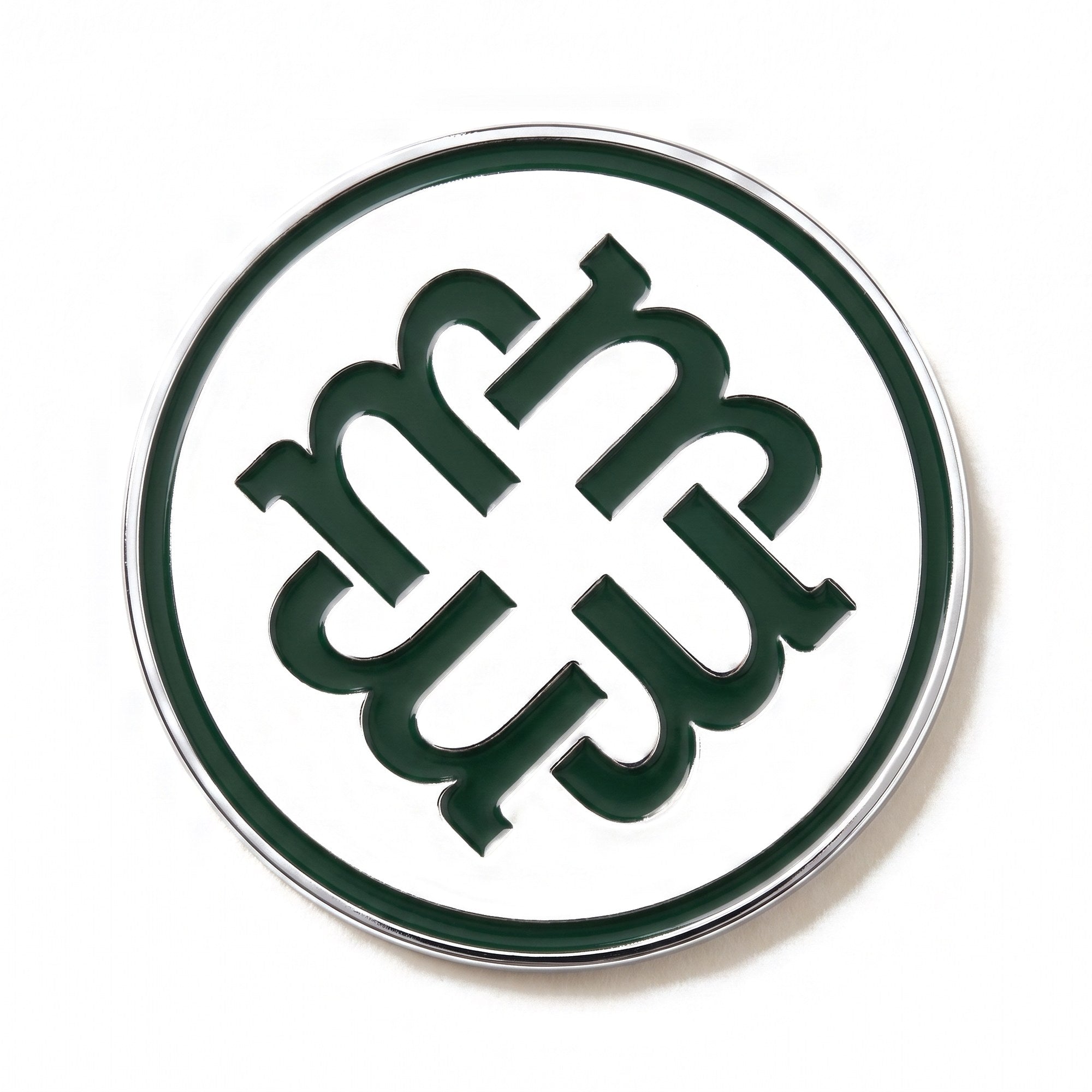 The Monogram golf ball marker photographed flat from above, showing the full chrome disc and green enamel monogram.