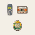 The Rewind ball marker set photographed flat from above on a cream background: a grey mobile phone, a cassette tape, an egg shaped handheld game, and the chrome Monogram Signature marker.