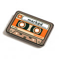 The Soundtrack golf ball marker, a taupe and orange cassette tape with marked handwritten on the label, photographed at an angle.