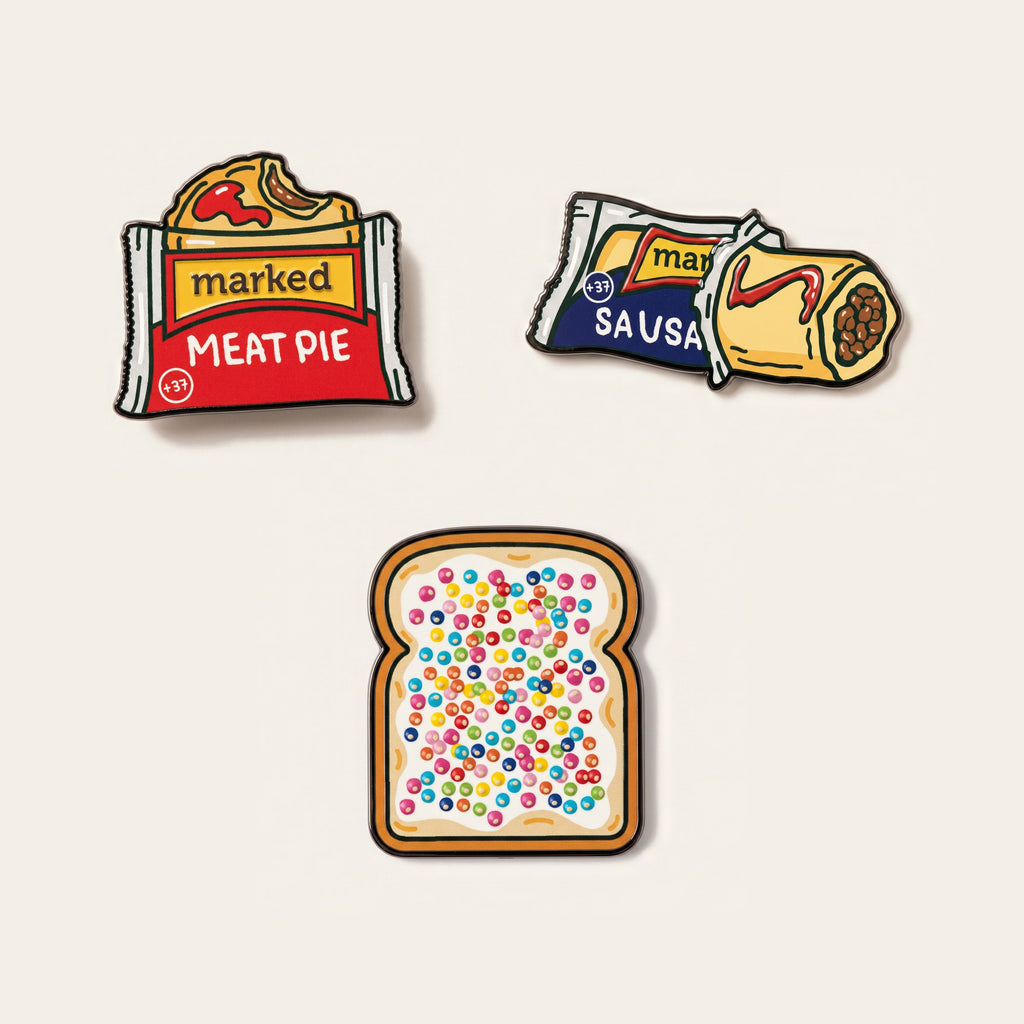 The Turn ball marker set photographed flat from above on a cream background: a wrapped meat pie, a sausage roll, a slice of fairy bread, and the chrome Monogram Signature marker.